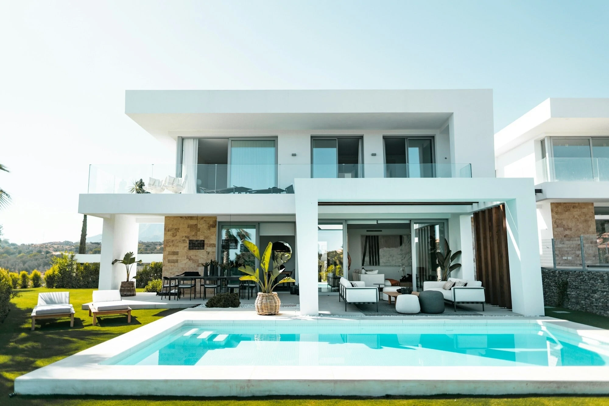 Big modern home, all white with big glass windows, outdoor living area with big pool.