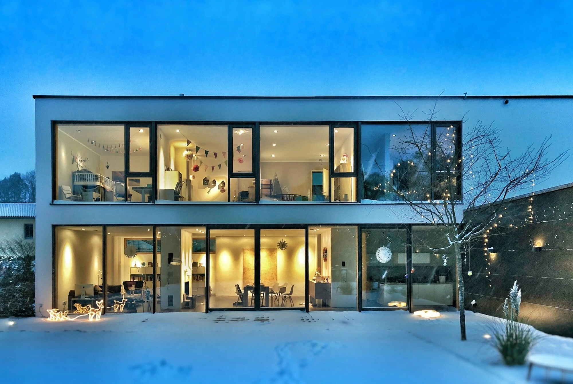 Fancy home,  white building with big glass windows on outside. All warm lights on inside.